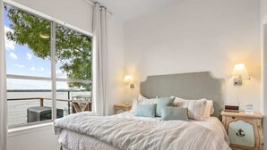 Une chambre avec un grand lit, deux tables de chevet, une vue sur l’eau et un balcon.