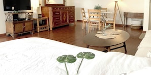 Habitación de hotel con cama, cómoda de madera, televisor, mesa de comedor con sillas y una planta pequeña.