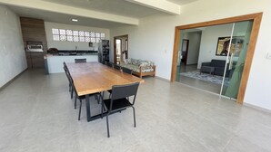 A spacious living area with a large wooden dining table, a sofa, and a glass partition. - Casa COMPLETA com Piscina 1 Min da Praia (Prado)