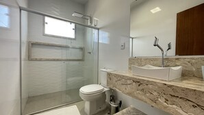 A modern bathroom with a glass shower enclosure, a white toilet, and a marble countertop with a sink. - Casa COMPLETA com Piscina 1 Min da Praia (Prado)