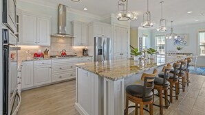 Una cocina amplia con armarios blancos, una isla grande con taburetes de bar, electrodomésticos de acero inoxidable e iluminación colgante.