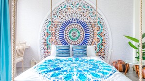 A bed with a patterned bedspread, a decorative headboard, and a small table with a plant. - Flying Club (Tainan)
