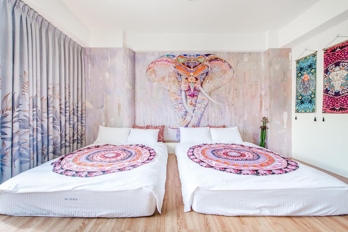 Une chambre avec deux lits, une grande tapisserie représentant un éléphant accrochée au mur et un cactus en pot.