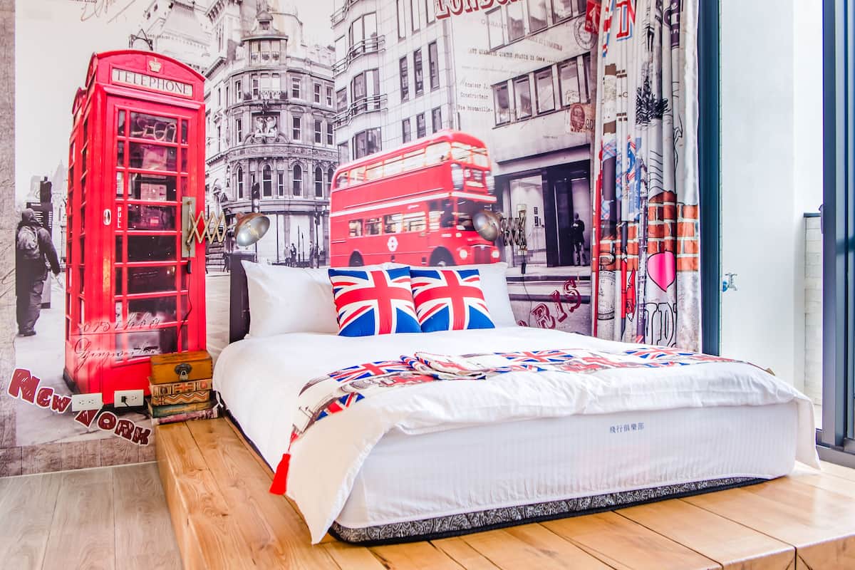 Une chambre avec un lit, une cabine téléphonique rouge et un autobus à deux étages.