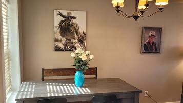Un comedor con una mesa de madera, cuatro sillas, un florero con flores y dos lámparas de pared.
