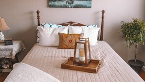 Een slaapkamer met een houten bed, een nachtkastje met een lamp, een lijst met een foto aan de muur, en een potplant.