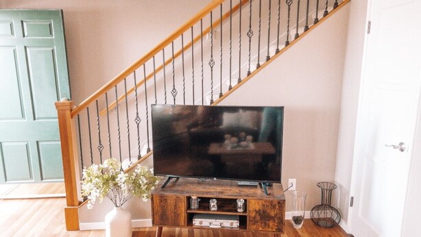 Een houten entertainmentkast met een flatscreen televisie, een trap met houten leuningen en een witte deur.