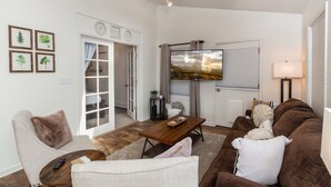 Un salon comprenant un canapé, un fauteuil, une table basse et un téléviseur. Une porte donne accès à un balcon.