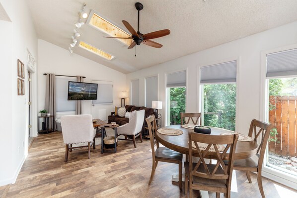 A spacious living room with a ceiling fan, a flat-screen TV, and a dining area with wooden furniture.