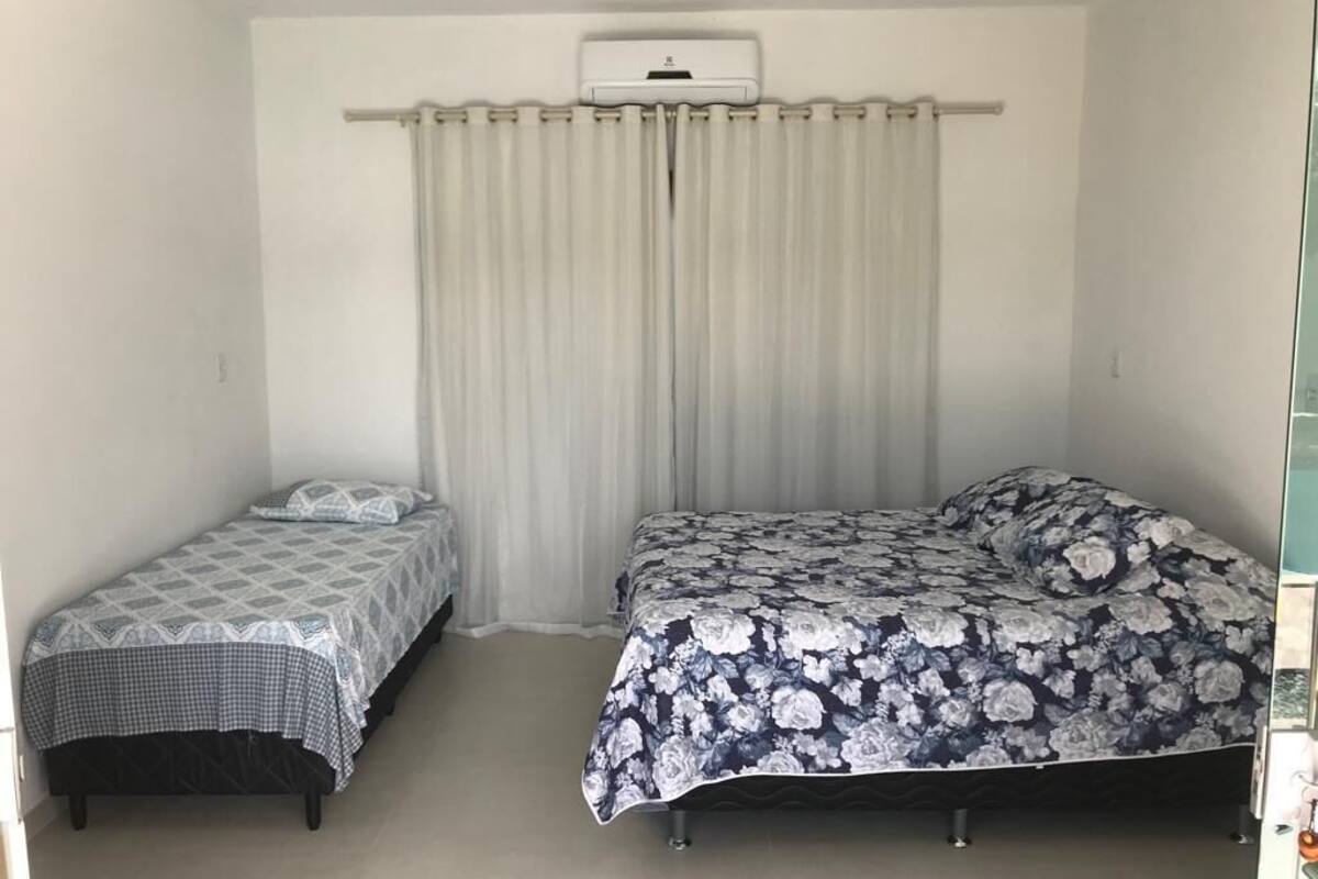A bedroom with two beds, a ceiling air conditioner, and a window with curtains.
