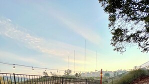 Uma área externa com espaço para sentar, incluindo fogueira, cadeiras e uma mesa, com vista para uma paisagem cercada e colinas ao longe.