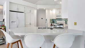 Uma cozinha moderna com armários brancos, uma ilha central com assentos e um forno embutido.