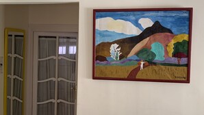 Ein Zimmer mit einer zum Balkon führenden Tür, einem Bild an der Wand und einem mit Vorhängen versehenen Fenster.