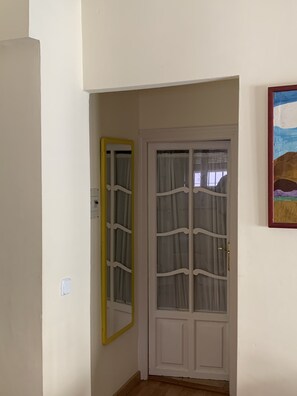 A hallway with a white door, a yellow-framed mirror, and a painting on the wall. - Céntrico y acogedor (Sevilla)