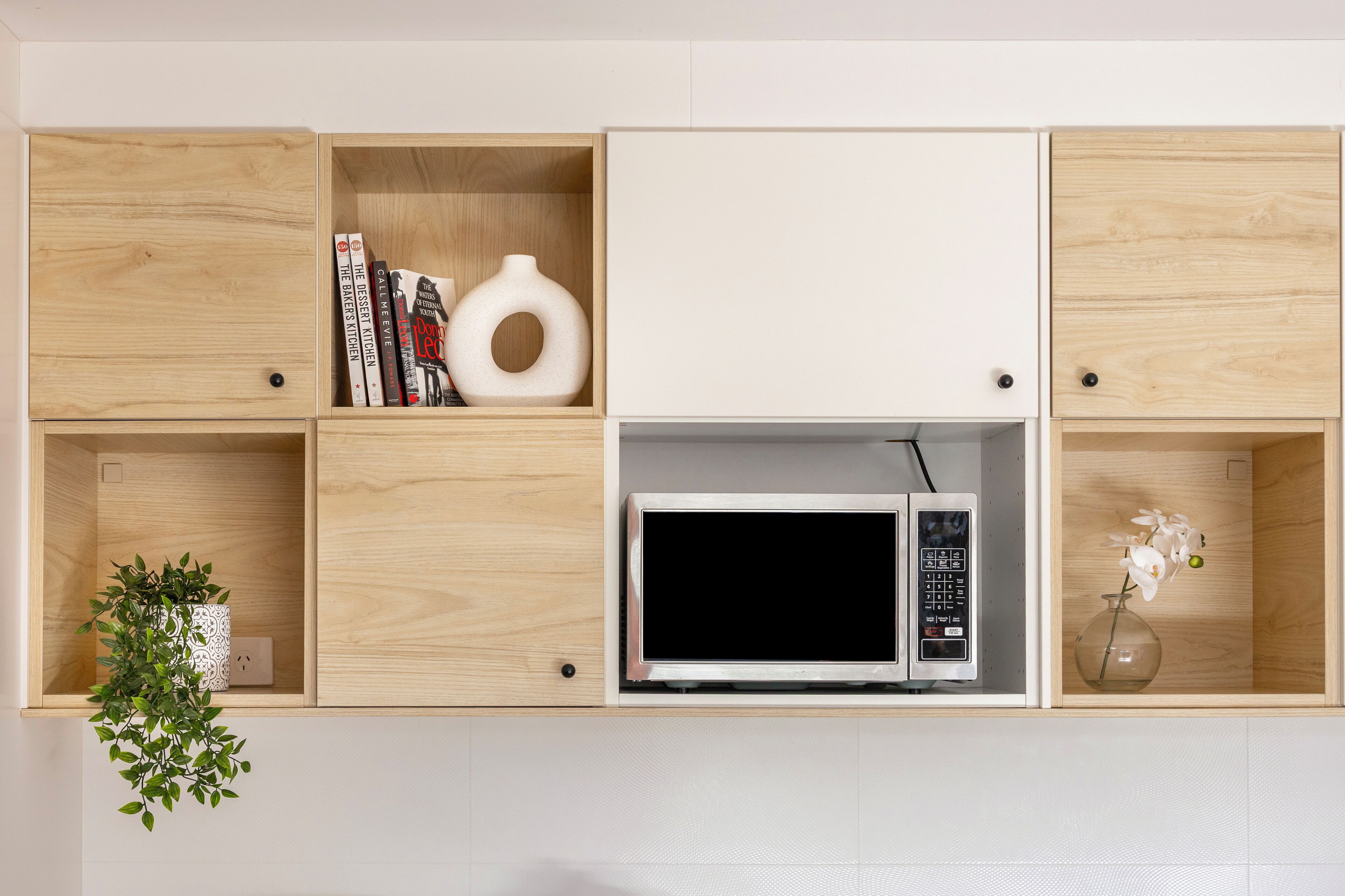 A wall-mounted wooden cabinet with multiple compartments, including a microwave, books, and decorative items.