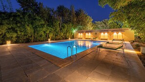 A swimming pool with a clear blue water surface, surrounded by a stone deck. There are two lounge chairs and a small table near the pool. - Jungle Cave Resort (Sawai Madhopur)