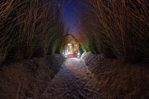 Un sendero estrecho que conduce a un edificio iluminado, rodeado de hierba alta.