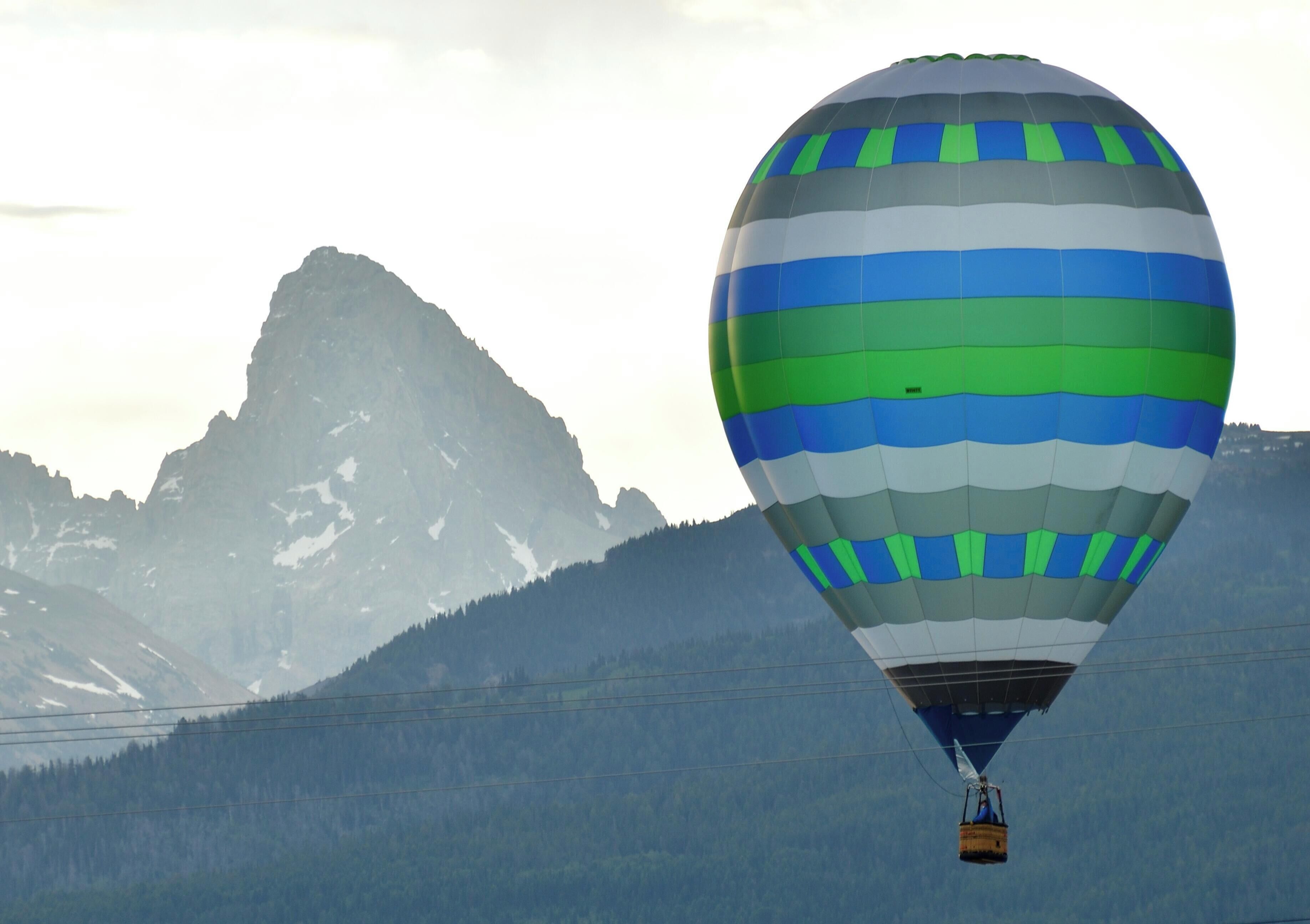 Eine Heißluftballon mit Streifenmuster über einer gebirgigen Landschaft.