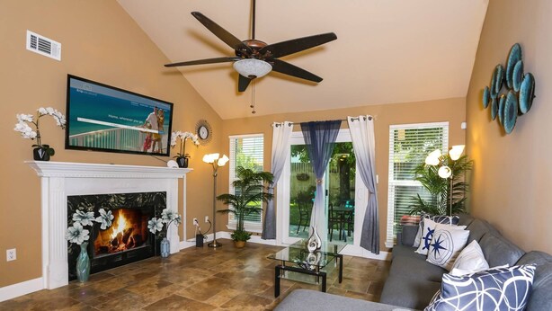A living room with a fireplace, a ceiling fan, a television, and a sofa. - Month Stays Available | Close to Hurlburt Field, Navarre & Okaloosa | Dogs Ok |Fenced Yard |Foosball (Mary Esther)