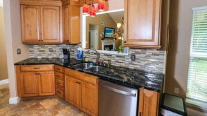 A kitchen with wooden cabinets, a black countertop, and a stainless steel dishwasher. - Month Stays Available | Close to Hurlburt Field, Navarre & Okaloosa | Dogs Ok |Fenced Yard |Foosball (Mary Esther)