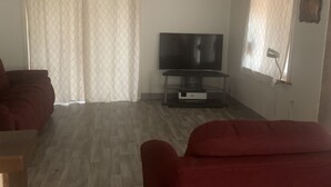 A living room with a flat-screen TV on a stand, a red sofa, and a wooden floor.