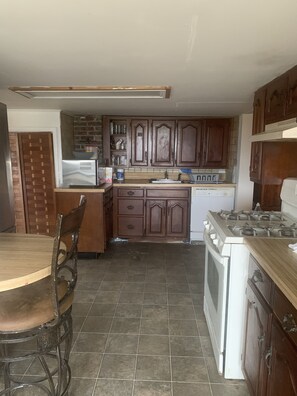 A kitchen with wooden cabinets, a stove, a sink, and a dining table with chairs.