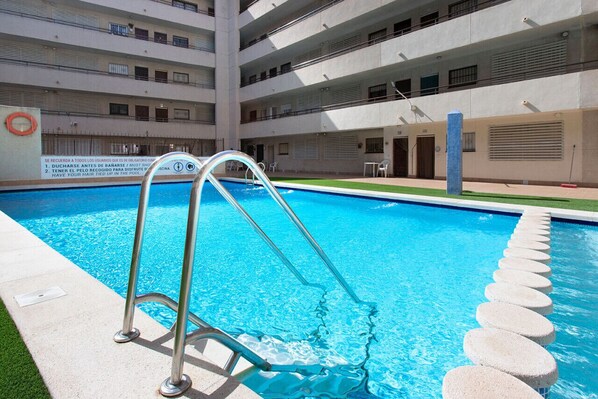 Ein Schwimmbecken mit einer Metallleiter, umgeben von einem mehrstöckigen Gebäude mit Balkonen.