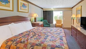 Habitación de hotel con una cama grande, un escritorio, una silla, un televisor y una ventana con cortinas.