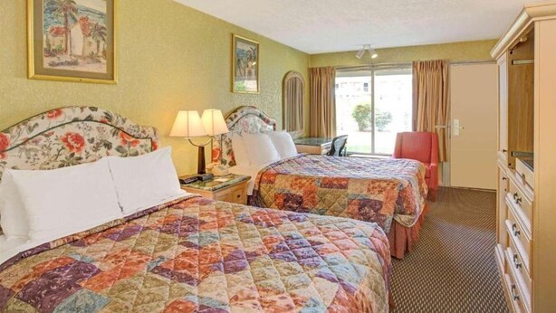 Habitación de hotel con dos camas, un aparador, una silla y un balcón con cortinas.