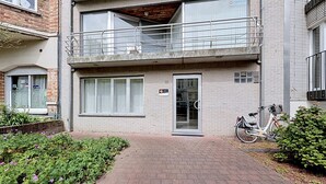 Ein zweistöckiges Gebäude mit Balkon, einem draußen abgestellten Fahrrad und einem kleinen Garten.