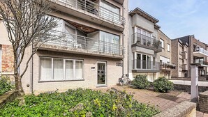 Ein mehrstöckiges Wohngebäude mit Balkonen, einer Ziegel-Fassade und einem Gartenbereich mit unterschiedlichen Pflanzen.
