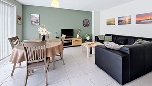 Ein Wohnzimmer mit Essbereich, einer schwarzen Couch, einem Fernseher und Kunstwerken an den Wänden.