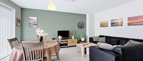 A living room with a dining area, a black sofa, a TV, and artwork on the walls.
