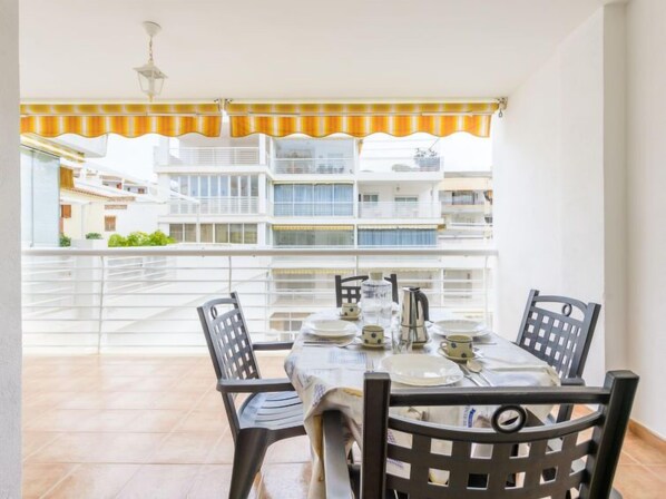 A balcony with a table set for four, chairs, and a view of residential buildings.