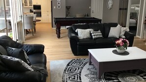 Ein modernes Wohnzimmer mit einer schwarzen Ledersofa, einem weißen Couchtisch und einem gemusterten Teppich. Im Hintergrund ist ein Essbereich mit einem weißen Tisch und Stühlen zu sehen.