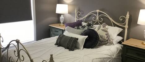 Un lit bien fait, avec une couette blanche et plusieurs oreillers, une tête de lit en métal blanche et deux tables de chevet avec des lampes.