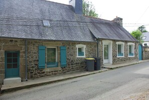 A stone building with a sloped roof, a front door, and windows with shutters.