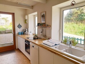 A kitchen with a large window, a sink, a kettle, and a dishwasher.