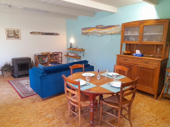 A living room with a blue sofa, a dining table with chairs, a wooden cabinet, and a fireplace.
