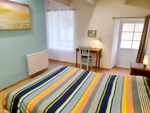 A bedroom with a bed, a chair, a desk, a radiator, a window with curtains, and a painting on the wall.
