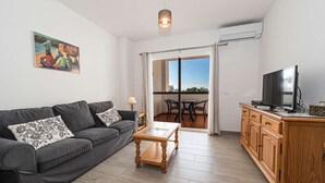 Ein Wohnzimmer mit grauem Sofa, einem Holztisch, einem Fernseher auf einer Holzkommode und einem Bild an der Wand.