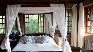 Habitación con cama con dosel, cortinas blancas y vistas a la vegetación a través de las ventanas.