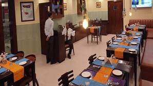 A restaurant with a modern interior, featuring a bar area, multiple dining tables, and a television screen displaying a news channel. - Hotel Comfort Inn Bl (Bareilly)