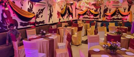 A banquet hall with round tables, chairs, and draped decorations.