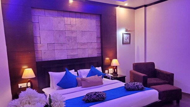 A modern hotel room with a large bed, a nightstand, a chair, and a decorative wall panel. - Hotel Comfort Inn Bl (Bareilly)