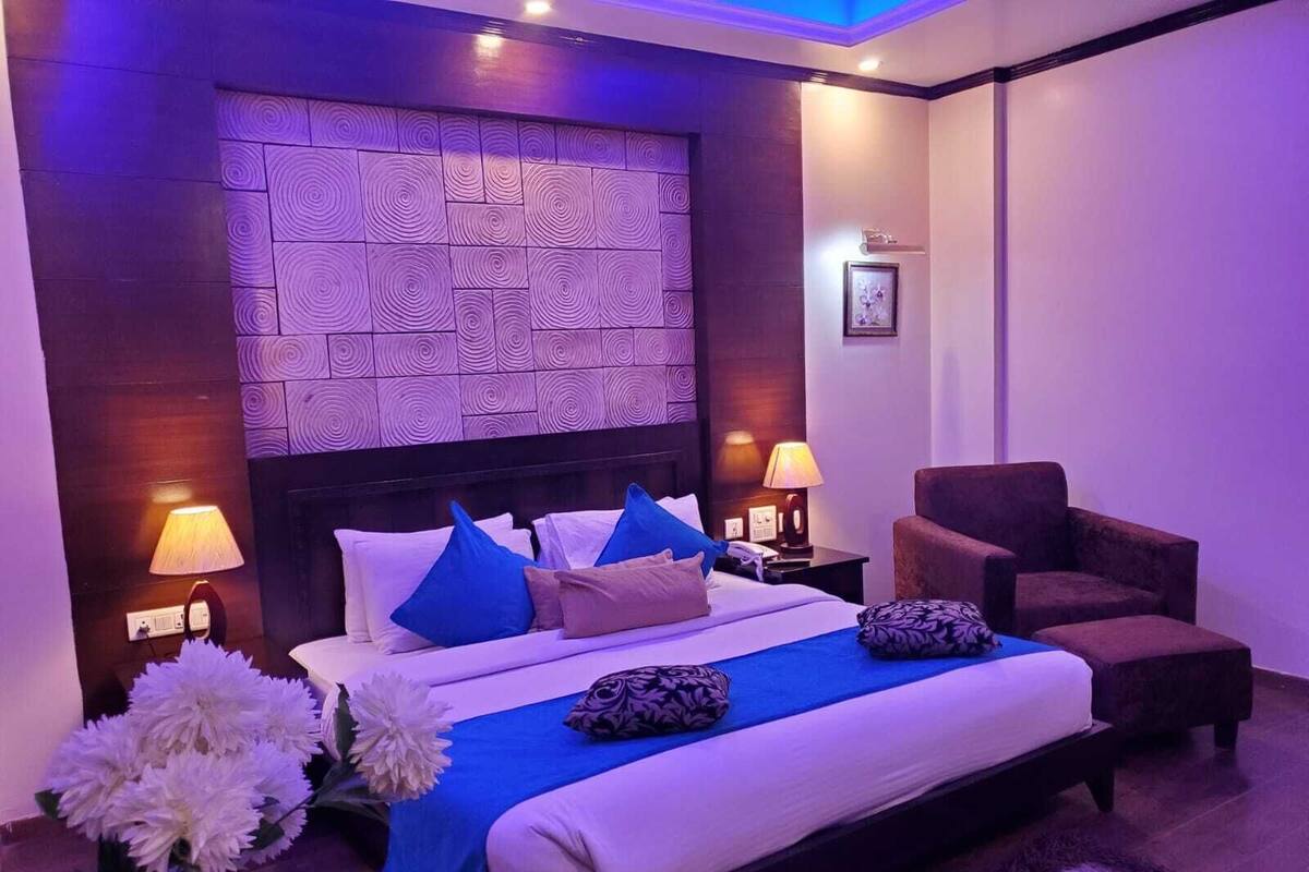 A modern hotel room with a large bed, a nightstand, a chair, and a decorative wall panel.