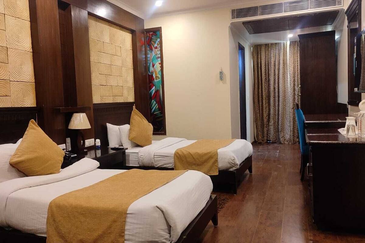 A hotel room with two beds, a desk, a chair, a TV, and a decorative wall panel.