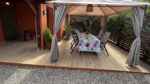 En udendørs patio med et bord dækket af en mønstret dug, omgivet af stole og et markise.