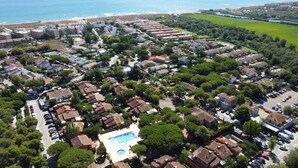 Oversigtsbillede af et boligområde med huse, en swimmingpool og en strand i baggrunden.
