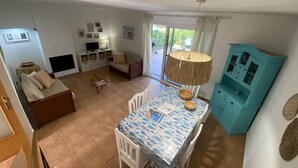 Una sala de estar con sofá, una mesa de comedor con sillas, televisor y lámpara.